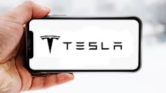 Hand, die ein Smartphone hält, auf dem das Logo des Unternehmens Tesla zu sehen ist; Symbolbild für die "Aktie im Fokus"
