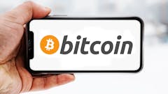 Hand, die ein Smartphone hält, auf dem das Logo des Unternehmens Bitcoin zu sehen ist; Symbolbild für die "Aktie im Fokus"