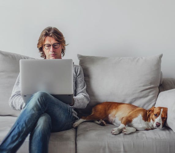 Mann mit Laptop und Hund auf Couch