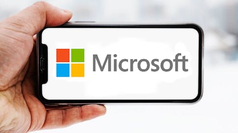 Hand, die ein Smartphone hält, auf dem das Logo des Unternehmens Microsoft zu sehen ist; Symbolbild für die "Aktie im Fokus"