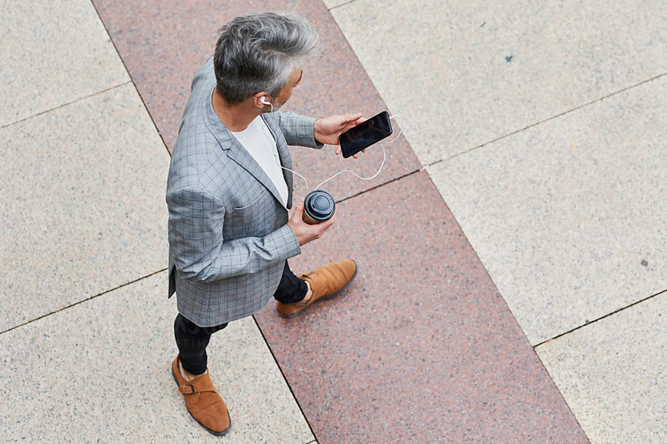 Mann auf Straße mit Mobiltelefon und Kaffee in der Hand