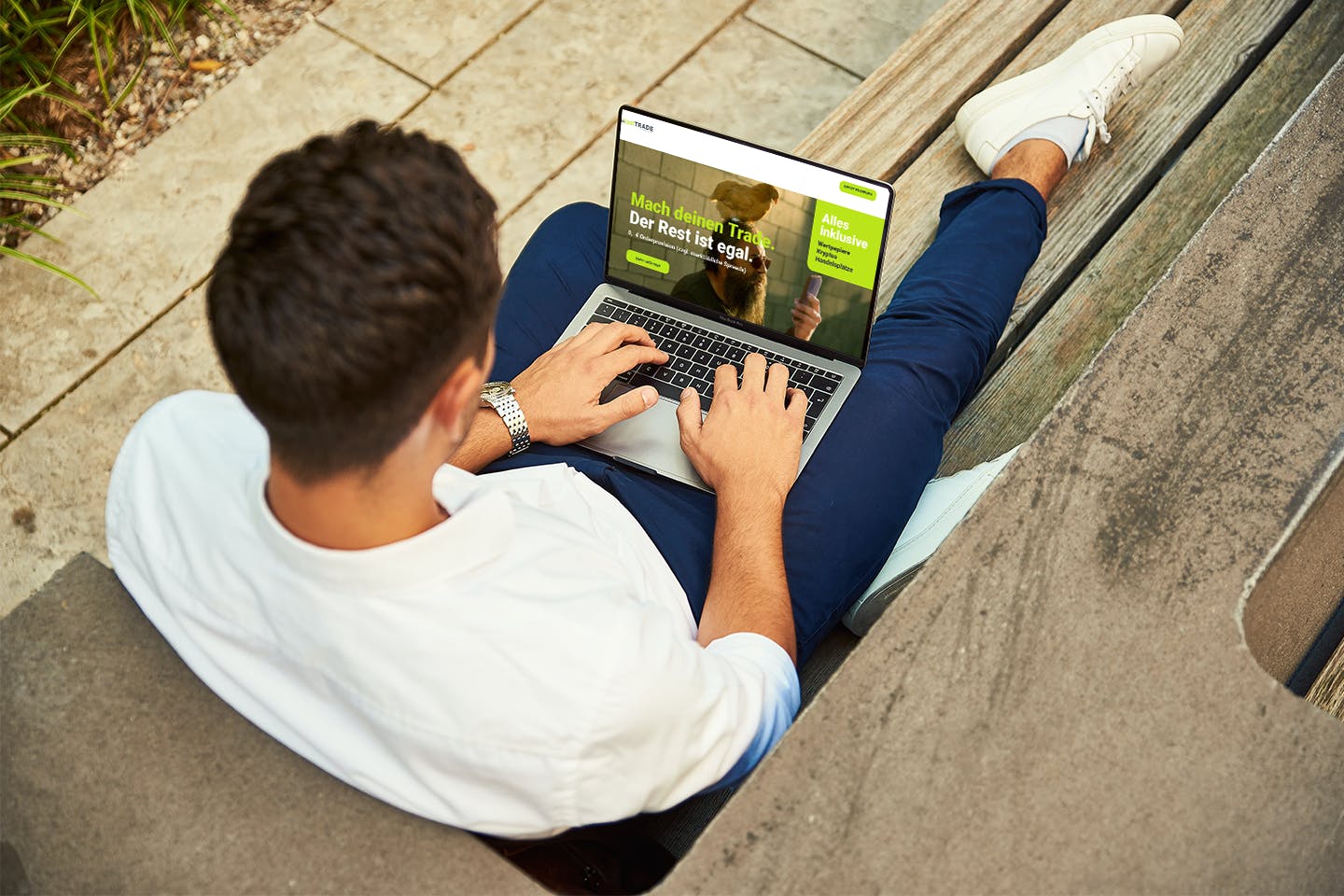 Junger Mann mit Laptop, der die Website von justTRADE darstellt, sitzt auf der Bank