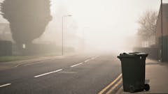 Straße im Nebel mit Mistkübel im Vordergrund