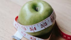ein Apfel, der mit einem Diät-Maßband abgemessen wird