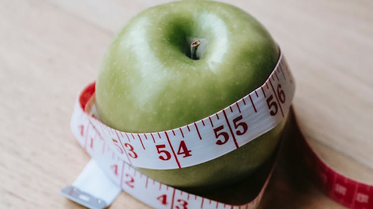 ein Apfel, der mit einem Diät-Maßband abgemessen wird